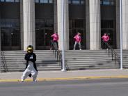 A few runners and a person in a penguin costume dance in front of the Civic Center.