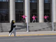 A few runners and a person in a penguin costume dance in front of the Civic Center.