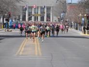 Runners make their way down the street as the race begins, with a few runners pulling ahead.