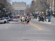 Runners make their way down the street as the race begins, with a few runners pulling ahead.