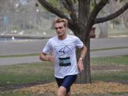 A runner in a white t-shirt and blue shorts continues towards the finish line