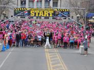 Runners line up at the start line of the race, most of them wearing pink race t-shirts