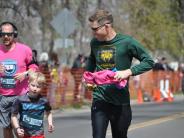 Several runners, including a father and child, are running towards the finish line