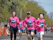 Several runners are shown running towards the finish line, each wearing a pink race t-shirt
