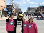 Three ladies in race t-shirts stand with the penguin mascot for a photo.