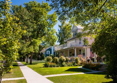 A sidewalk with houses on the right side and trees in the yards